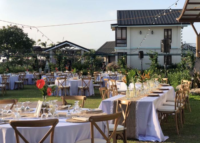 Outdoor event setup with tables, chairs, and decorations on a lawn. A white building is in the background.