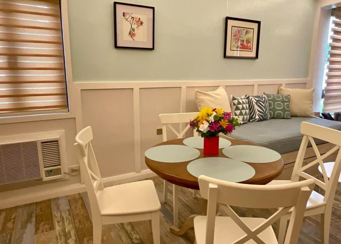 Cozy dining area with round table, white chairs, and floral centerpiece. Light blue wall and window blinds.