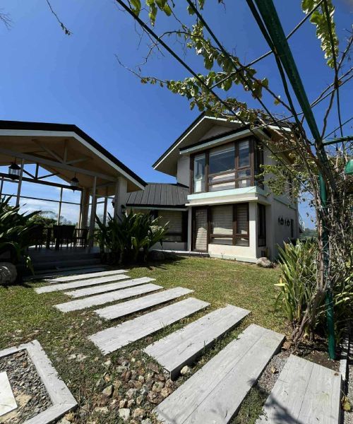 Two-story house with patio, pathway, and lush green lawn under a blue sky.