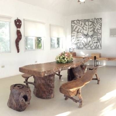 Rustic wooden dining table and chairs in a white-walled room with large artwork and windows.