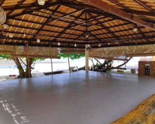 Open-air pavilion with thatched roof, concrete floor, near a beach. Natural light, simple decor.