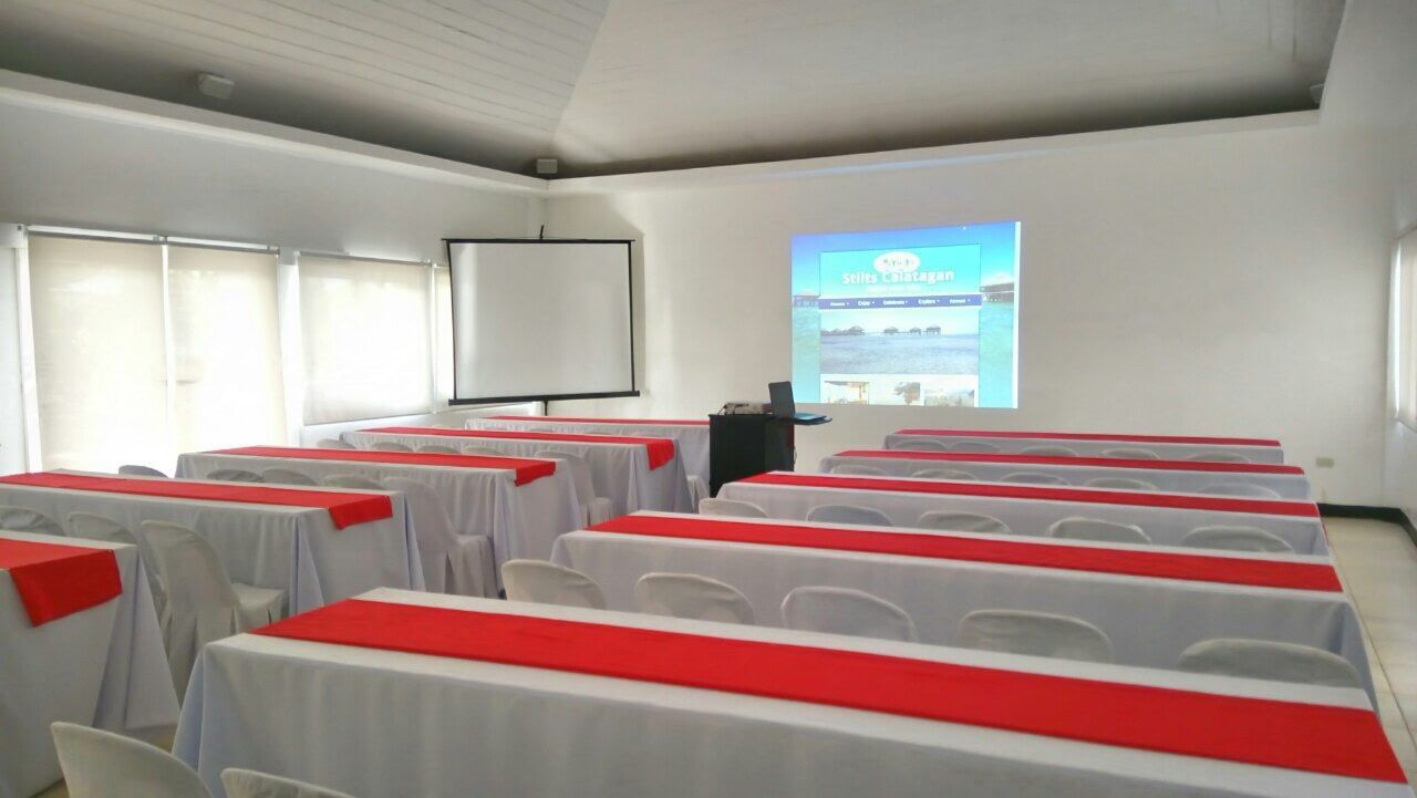 Conference room with white tables and red runners, projector screens, and chairs.