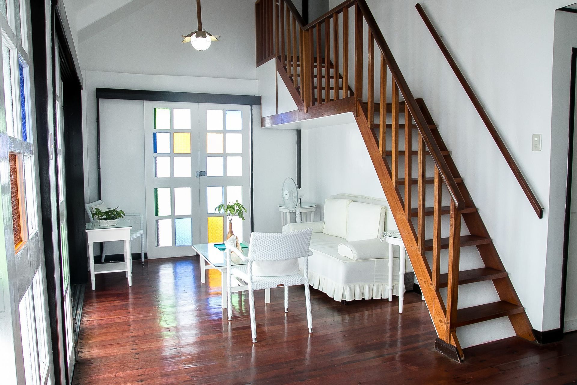 Interior with stairs, white furniture, and stained glass windows. Wooden floors, a light fixture, and a white doorway.