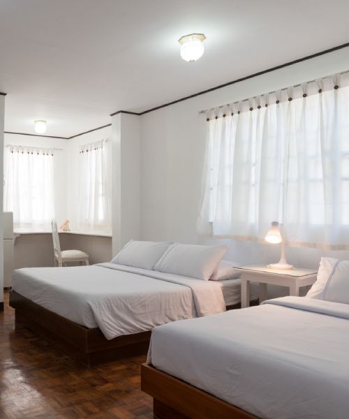 Bright white bedroom with three beds and a desk.