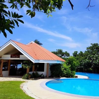 A resort building with a terracotta roof next to a blue pool on a sunny day.