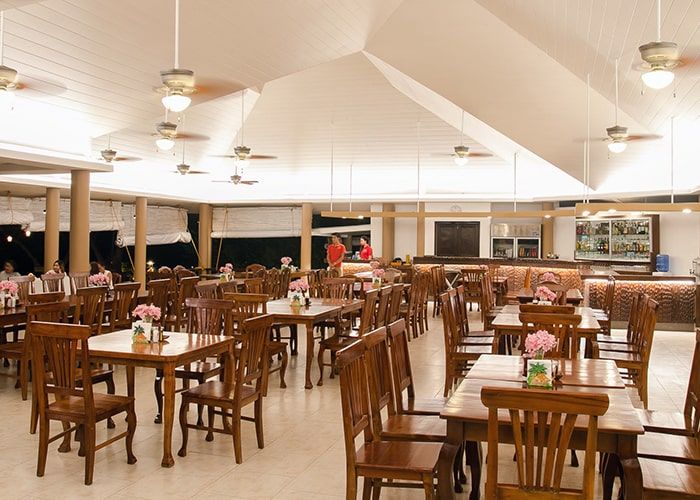 Restaurant interior with wooden tables and chairs, white ceilings, and a bar area.