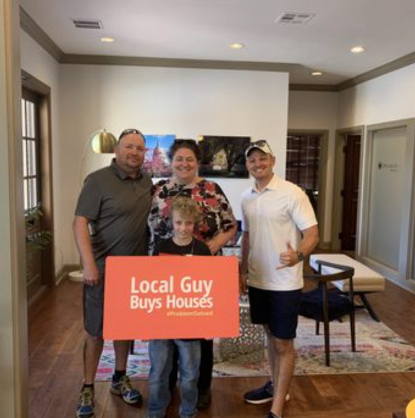 Family and Local Guy holding sign; celebrating a house purchase in an office.