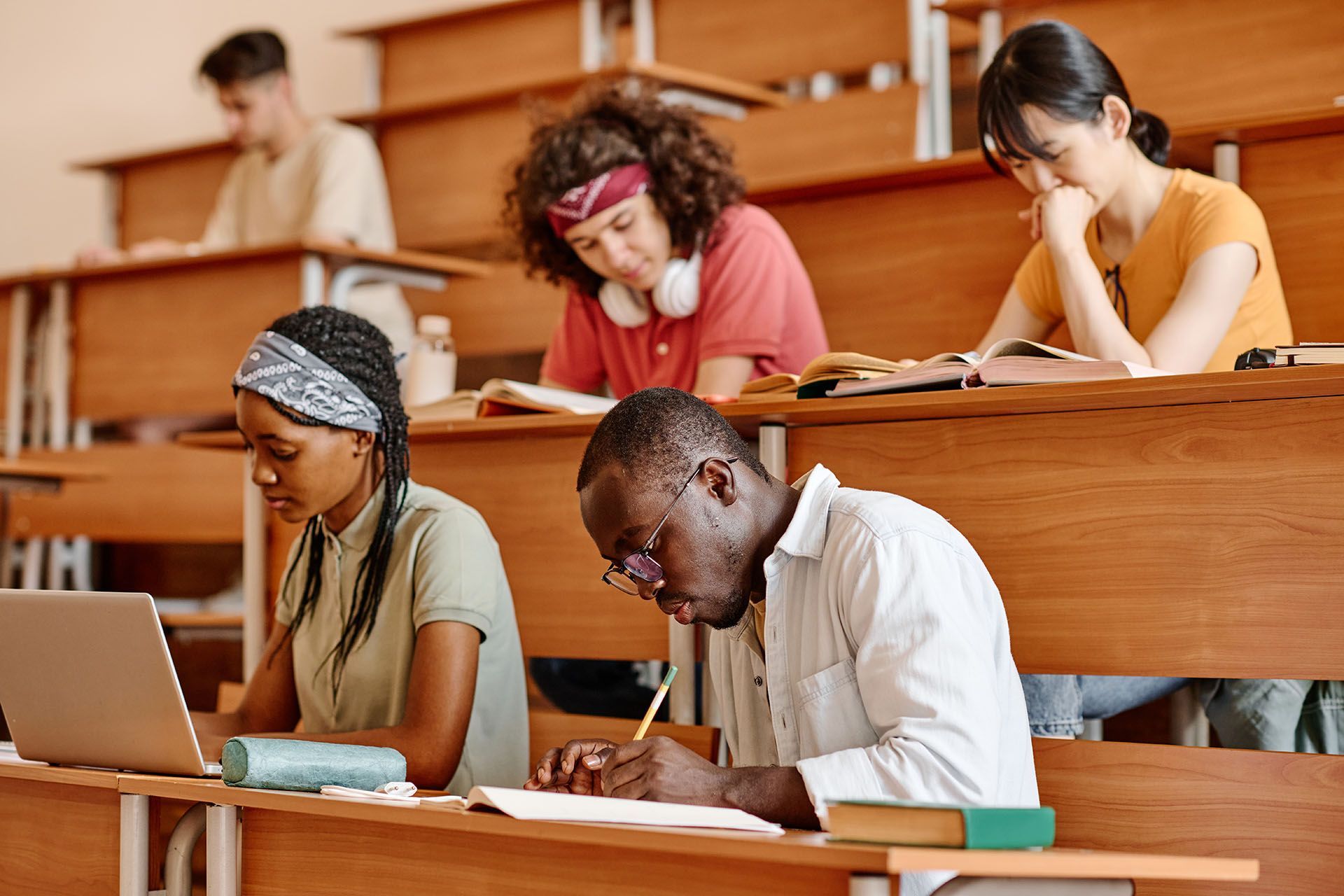 Students in a lecture hall taking notes, some with books and laptops.