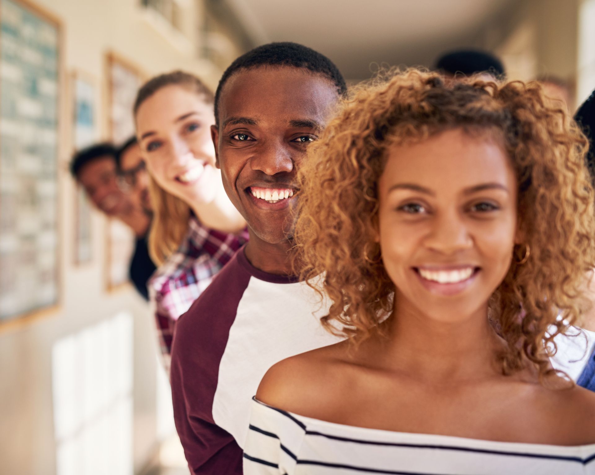 Group of smiling people in a hallway, looking towards the camera.