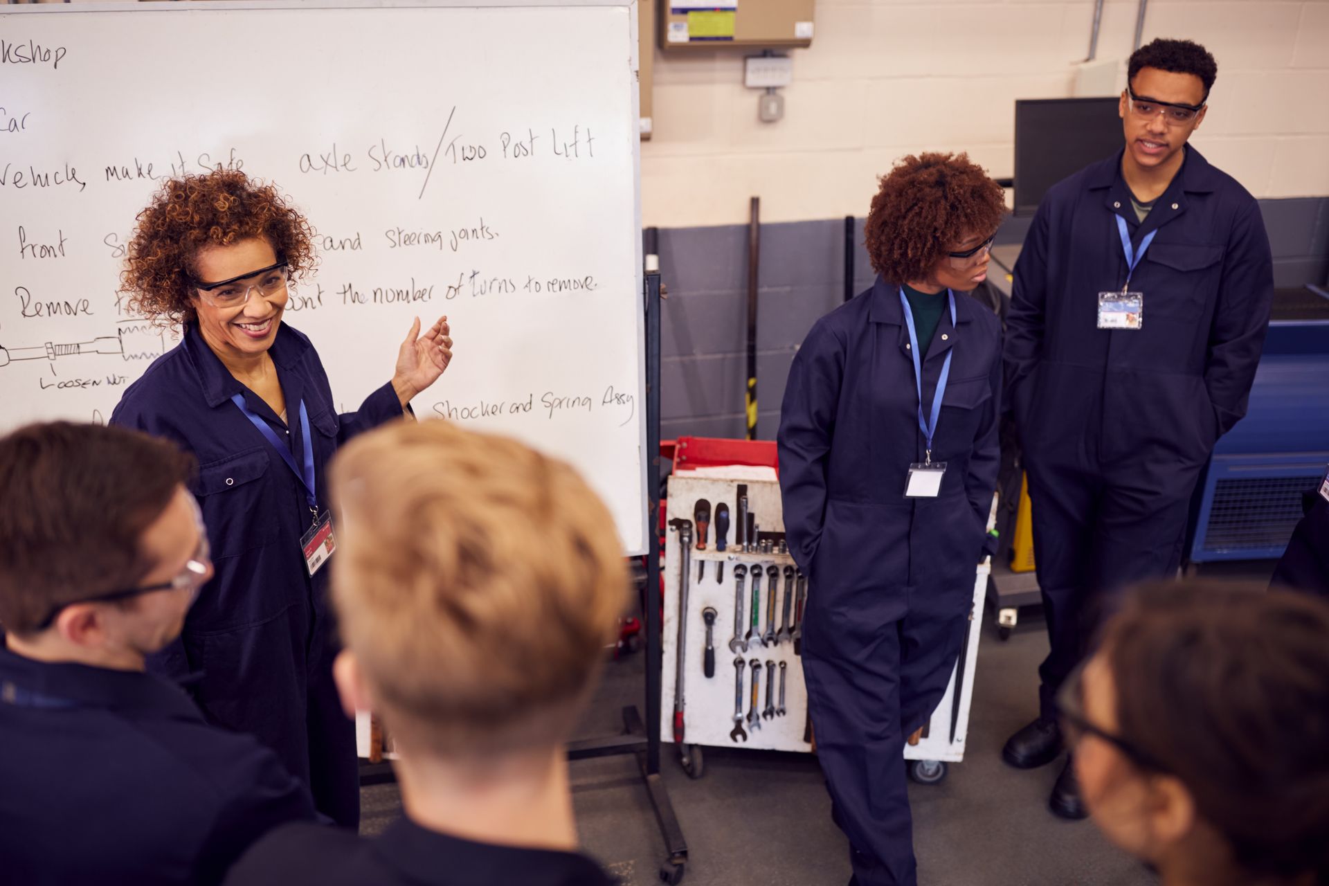 Mechanic instructor explaining whiteboard notes to students in workshop.