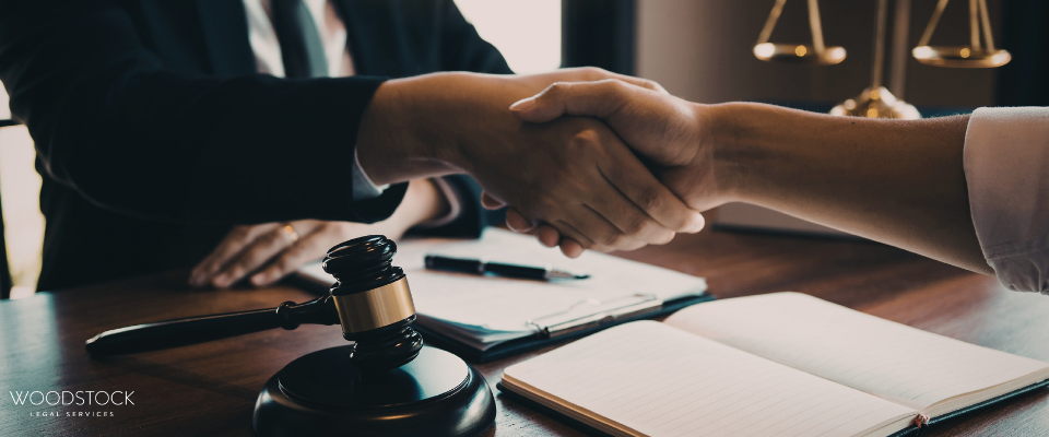 Professional handshake over a desk with a judge’s gavel, documents, and scales of justice in the background, symbolising a legal agreement or settlement.