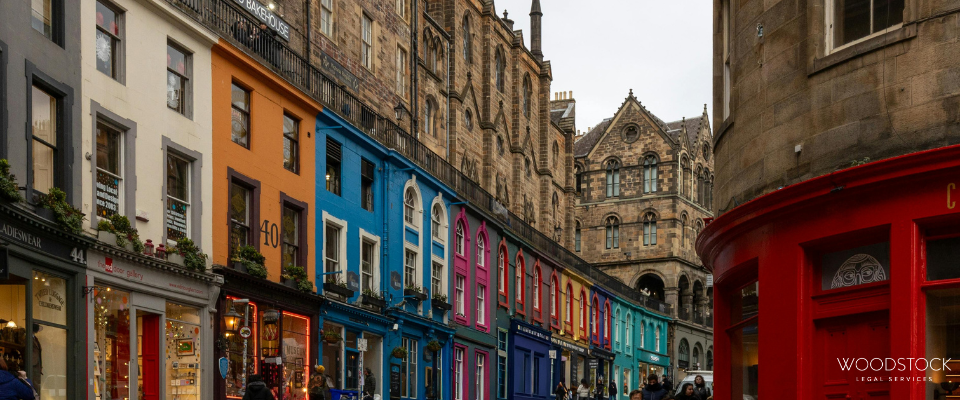 Colourful row of vibrant shopfronts along Victoria Street in Edinburgh with historic stone buildings and pedestrians walking on a curved cobbled street.