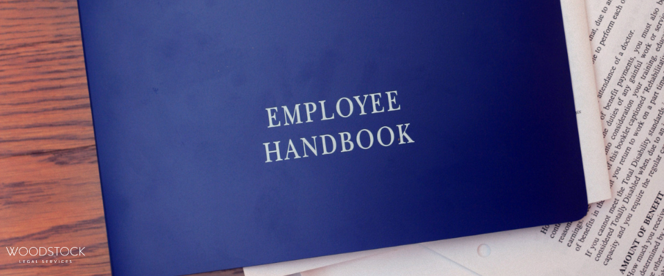Blue employee handbook folder placed on top of printed documents on a wooden desk.