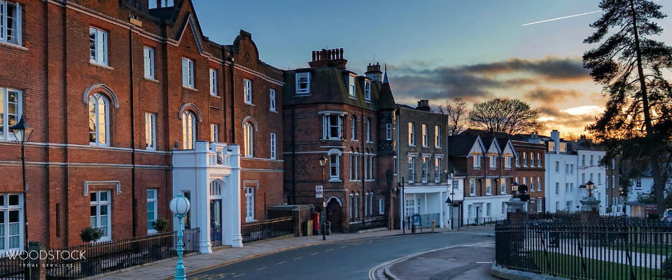 Red-brick historic buildings along a curved street at sunset, with Woodstock Legal Services in the foreground.