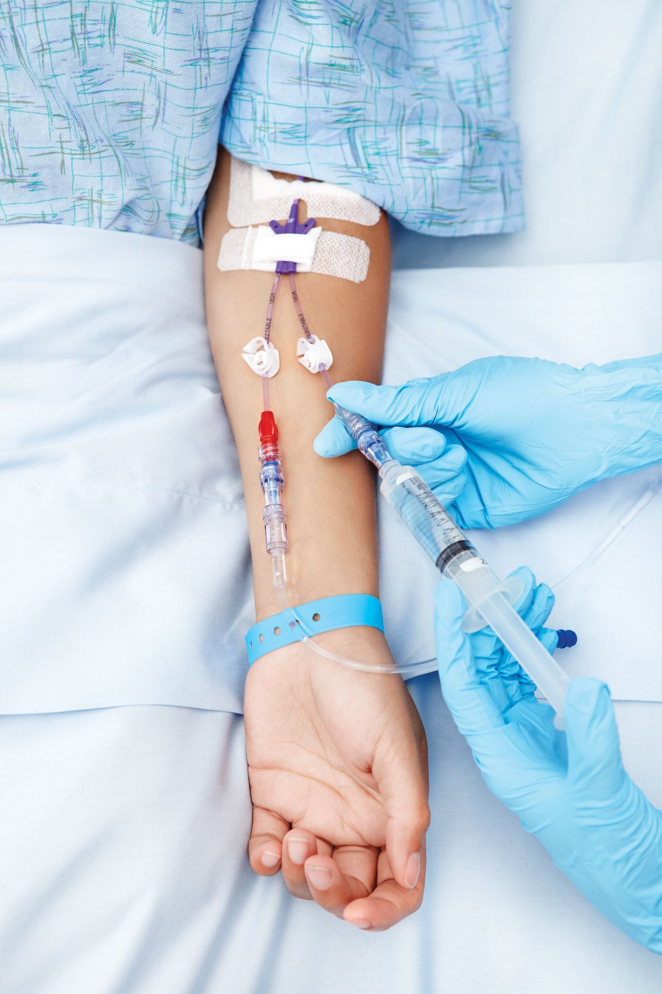 Gloved hand inserting IV into patient’s forearm in a hospital bed