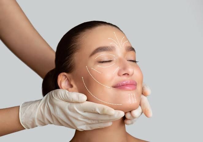 Gloved hands massage a woman’s face with cream, eyes closed and relaxed.