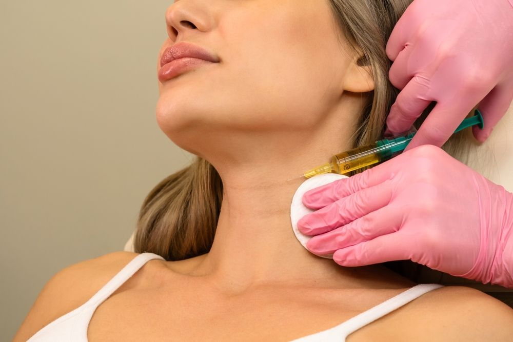 Healthcare worker injecting filler into a woman's neck with a syringe, wearing pink gloves