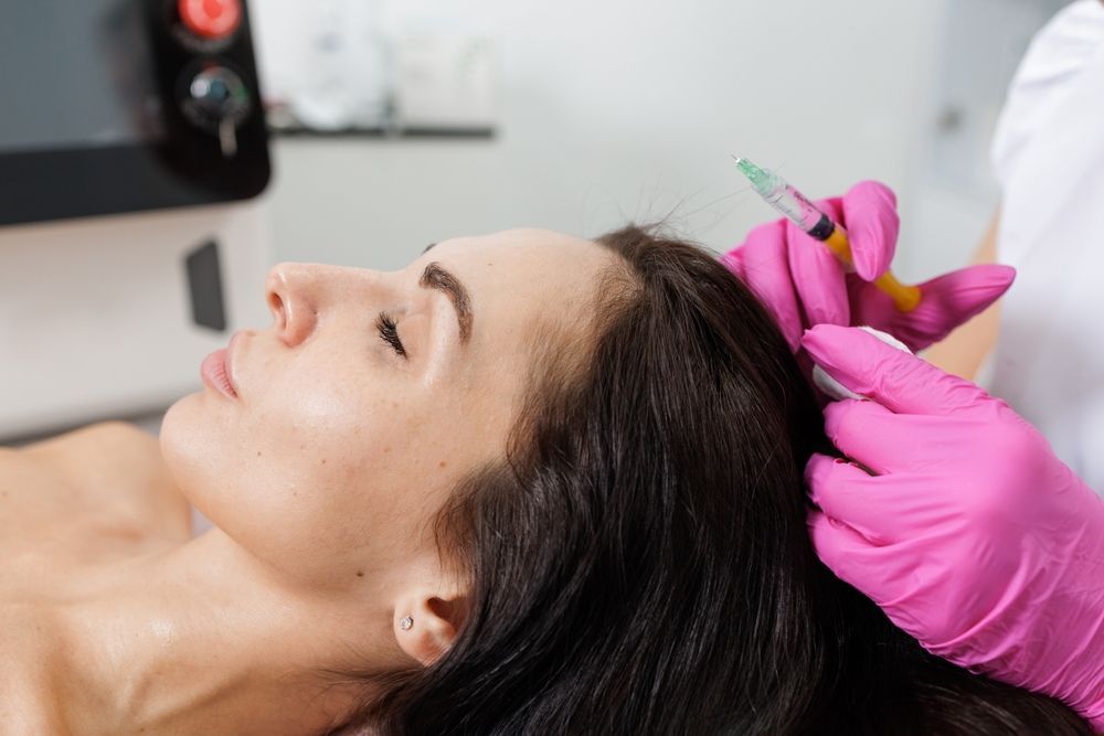 Woman receiving a pink flower hair treatment while lying back on a spa bed