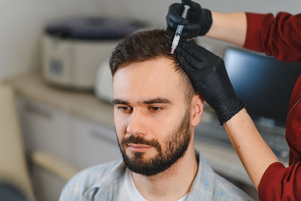 Stylist applying hair dye to a seated man in a salon