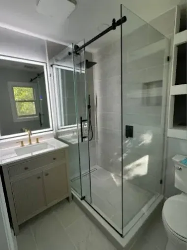 A modern bathroom featuring a vanity with gold fixtures, a walk-in glass shower with black hardware, and a white toilet.