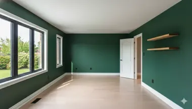 An empty room with dark green walls, light wood floors, a window, an open white door, and two floating wooden shelves.