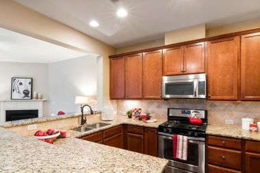 A kitchen with wood cabinets, granite countertops, stainless steel appliances, and a pass-through to a living area.