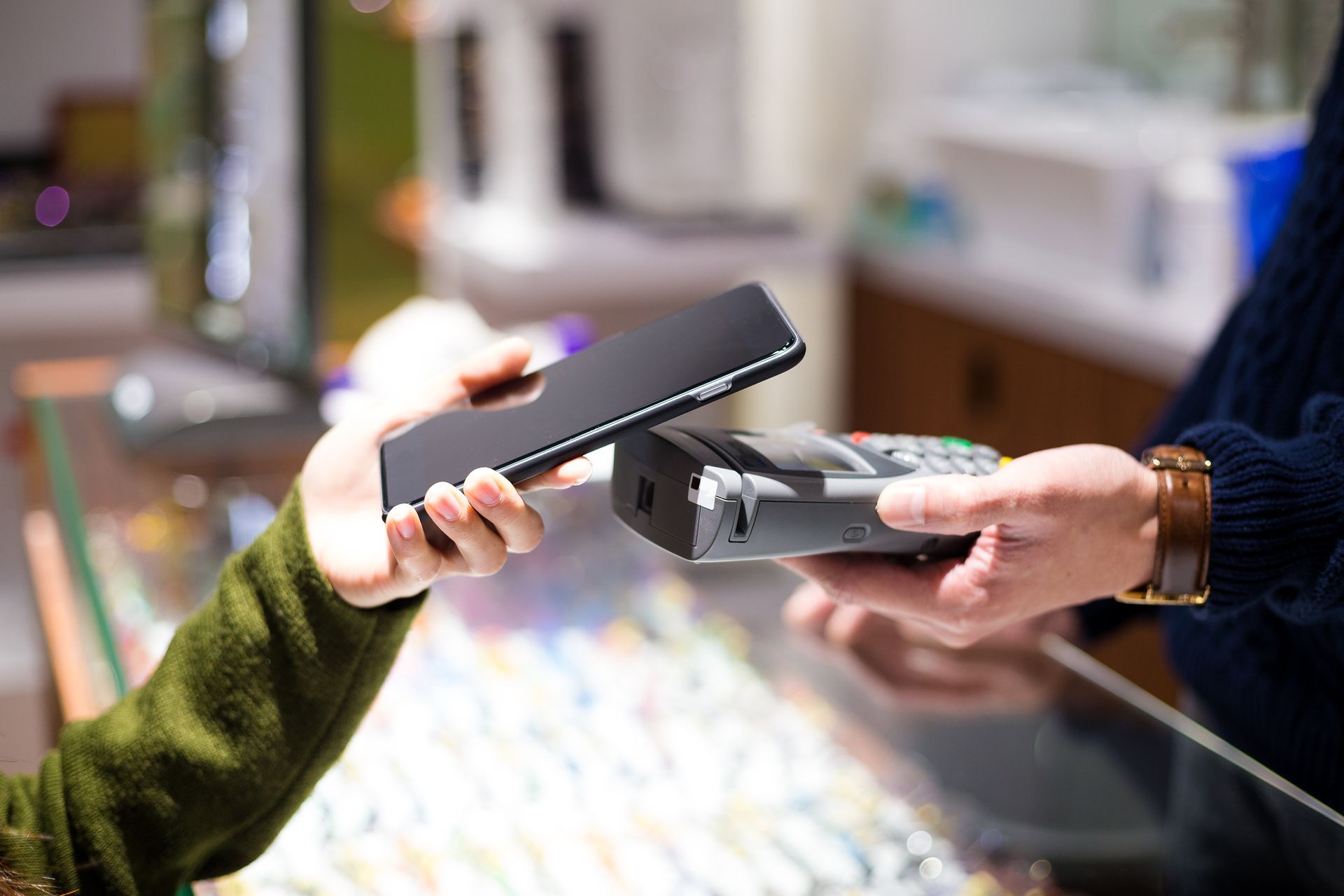 Hands exchanging a black card reader and a payment card at a checkout counter