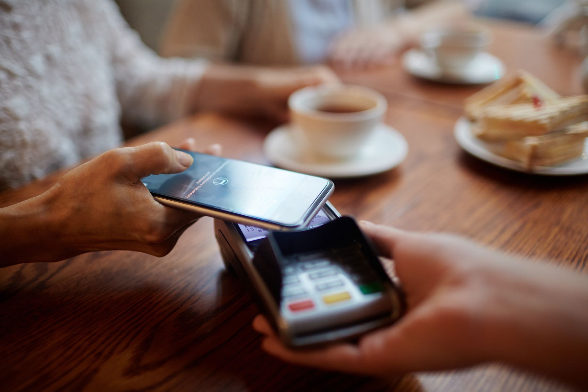 Hands using a smartphone for contactless payment at a café table with coffee and pastries