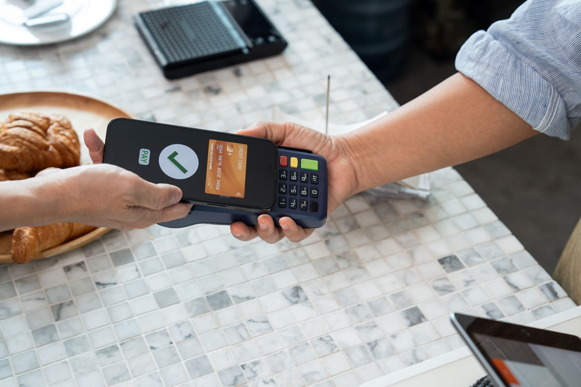 Person taps a card on a payment terminal at a café table with pastries and a laptop nearby