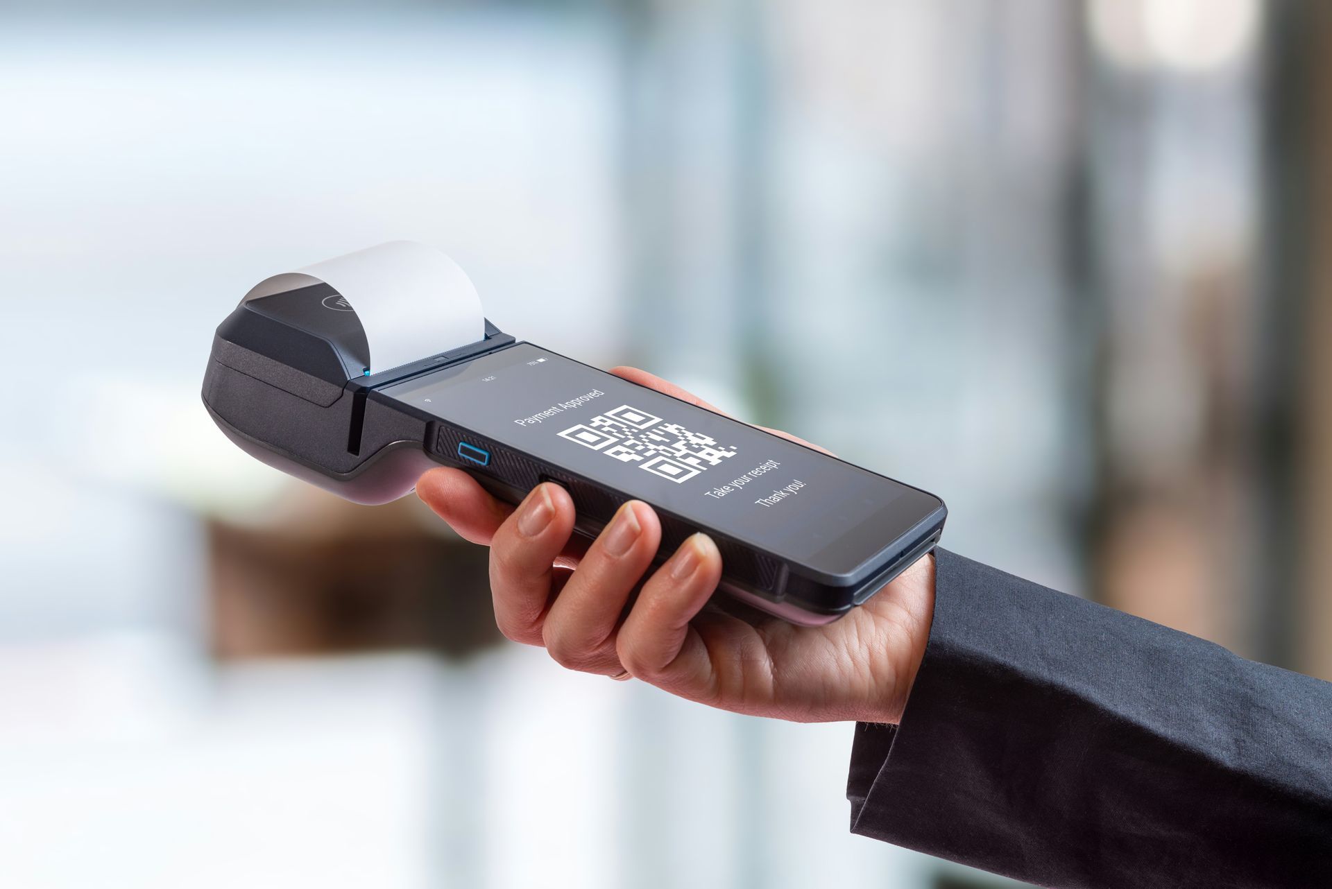 Hand holding a black payment terminal with a receipt coming out