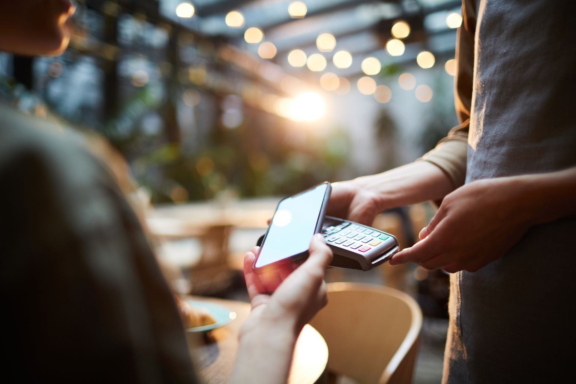 Person holding a smartphone near a payment terminal in a softly lit outdoor setting