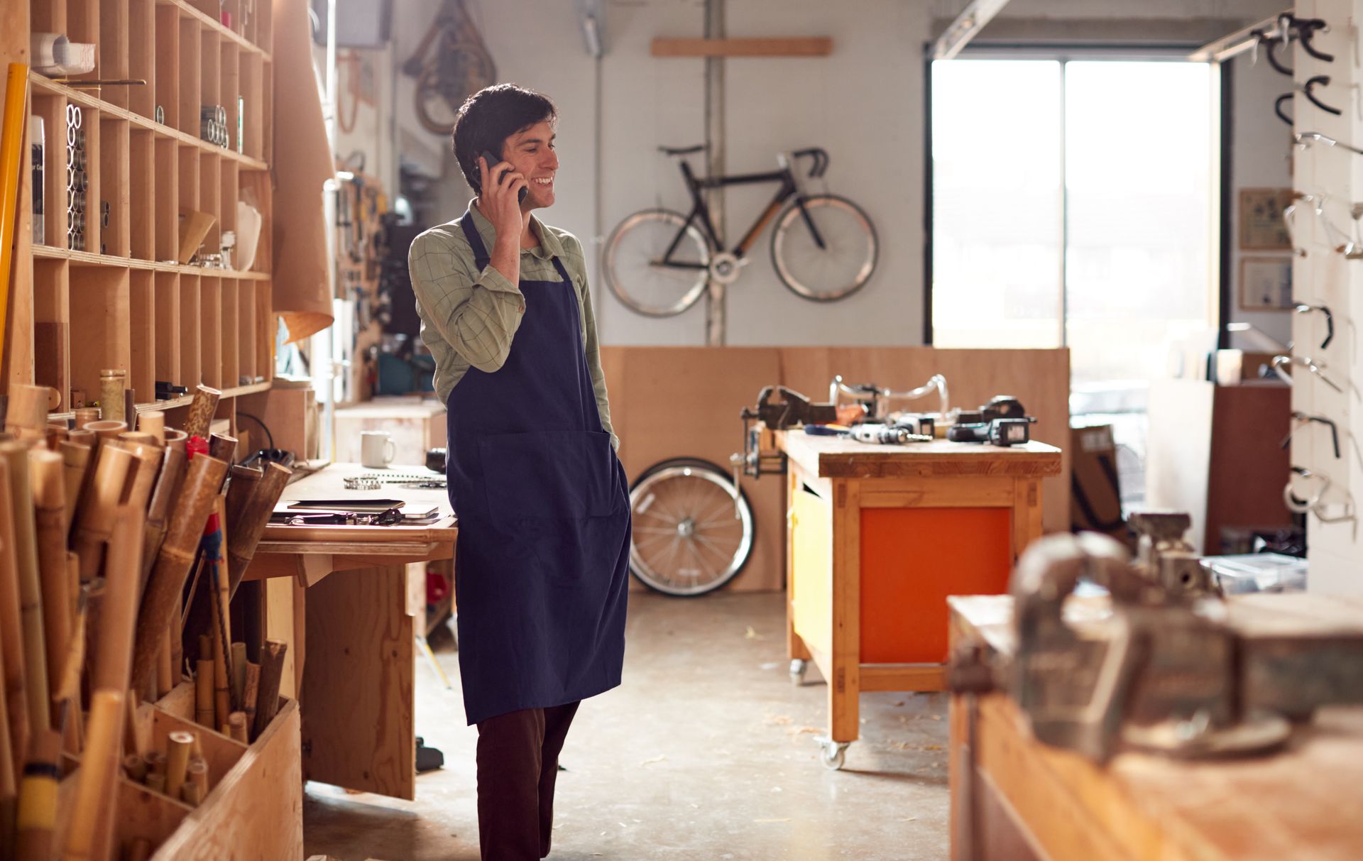 Person standing in a woodworking shop beside benches, tools, and a bicycle.