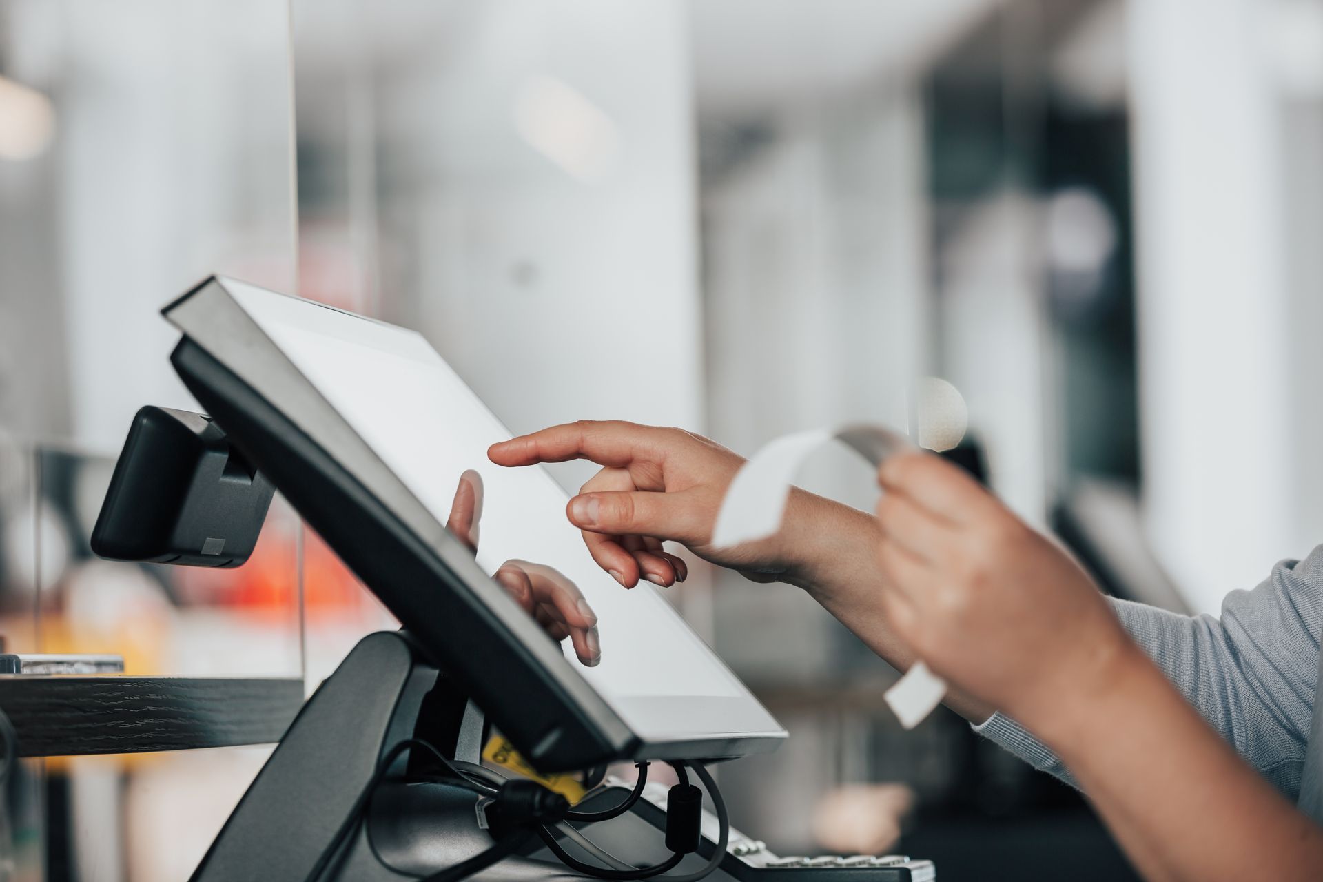 Hands using a touchscreen POS terminal in a bright retail checkout area