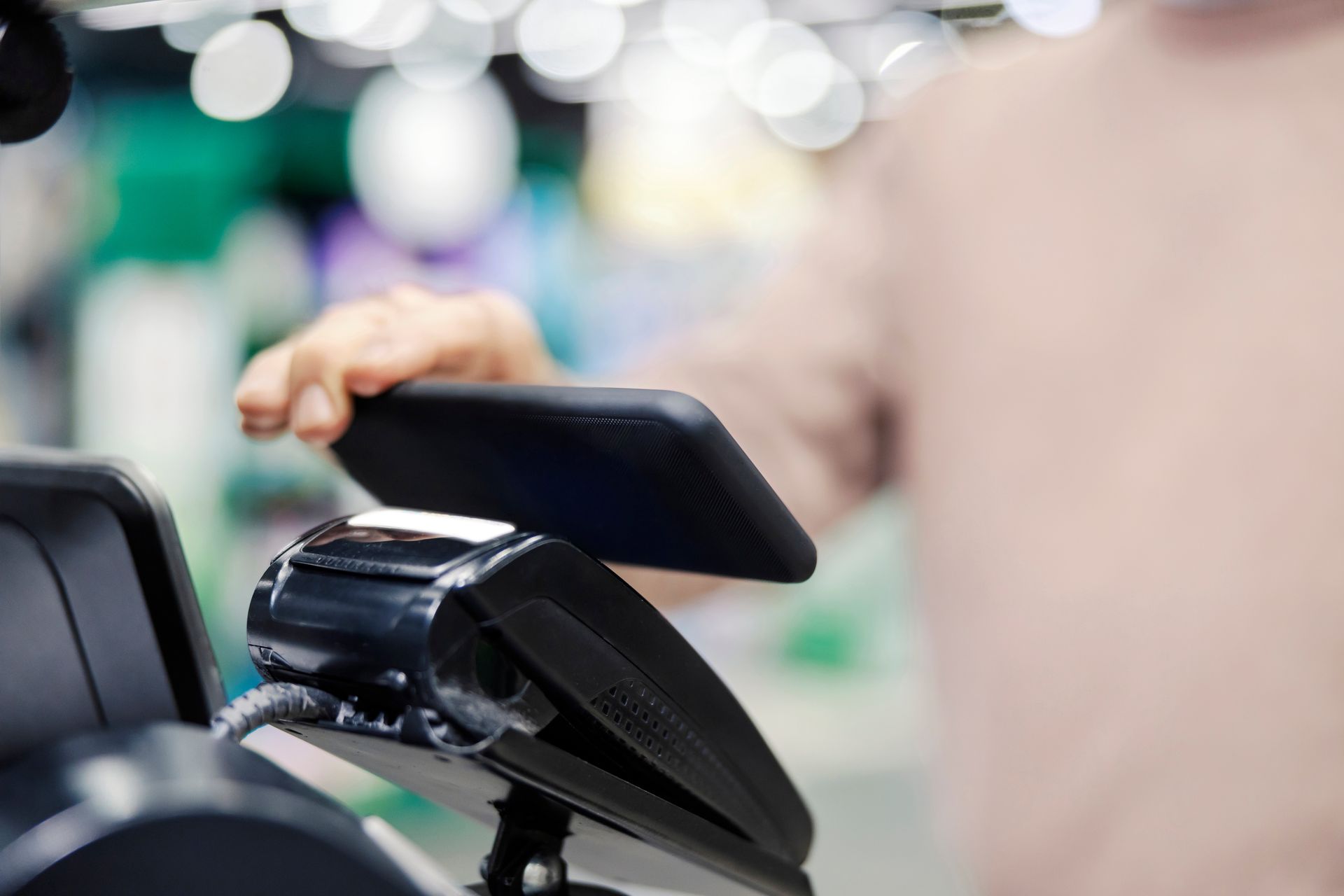 Person tapping a payment terminal in a store checkout line