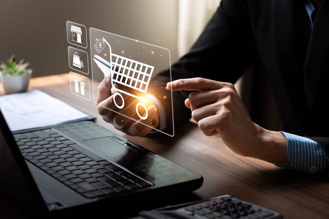 Person using a laptop and touching a transparent shopping cart icon on a digital screen interface