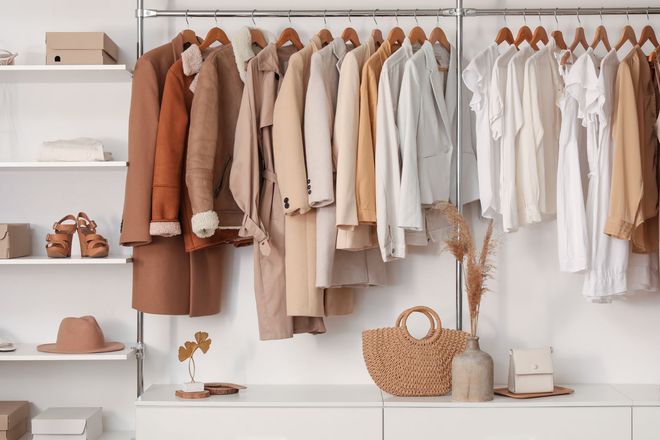Neutral-toned clothing rack in a minimalist boutique with coats, shirts, hats, and woven baskets on shelves