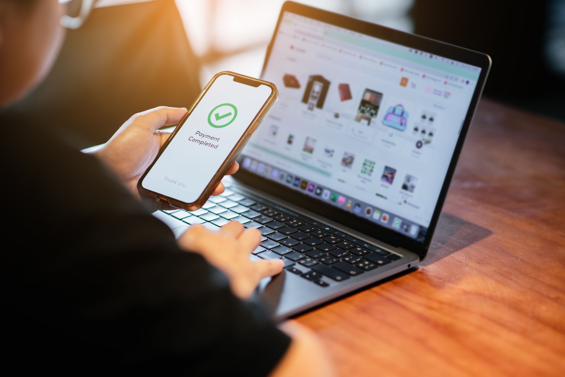 Person holding a phone with a green checkmark beside a laptop showing an online shopping page
