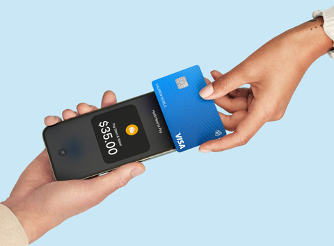 Hand holding a smartphone above a card payment terminal at a checkout counter