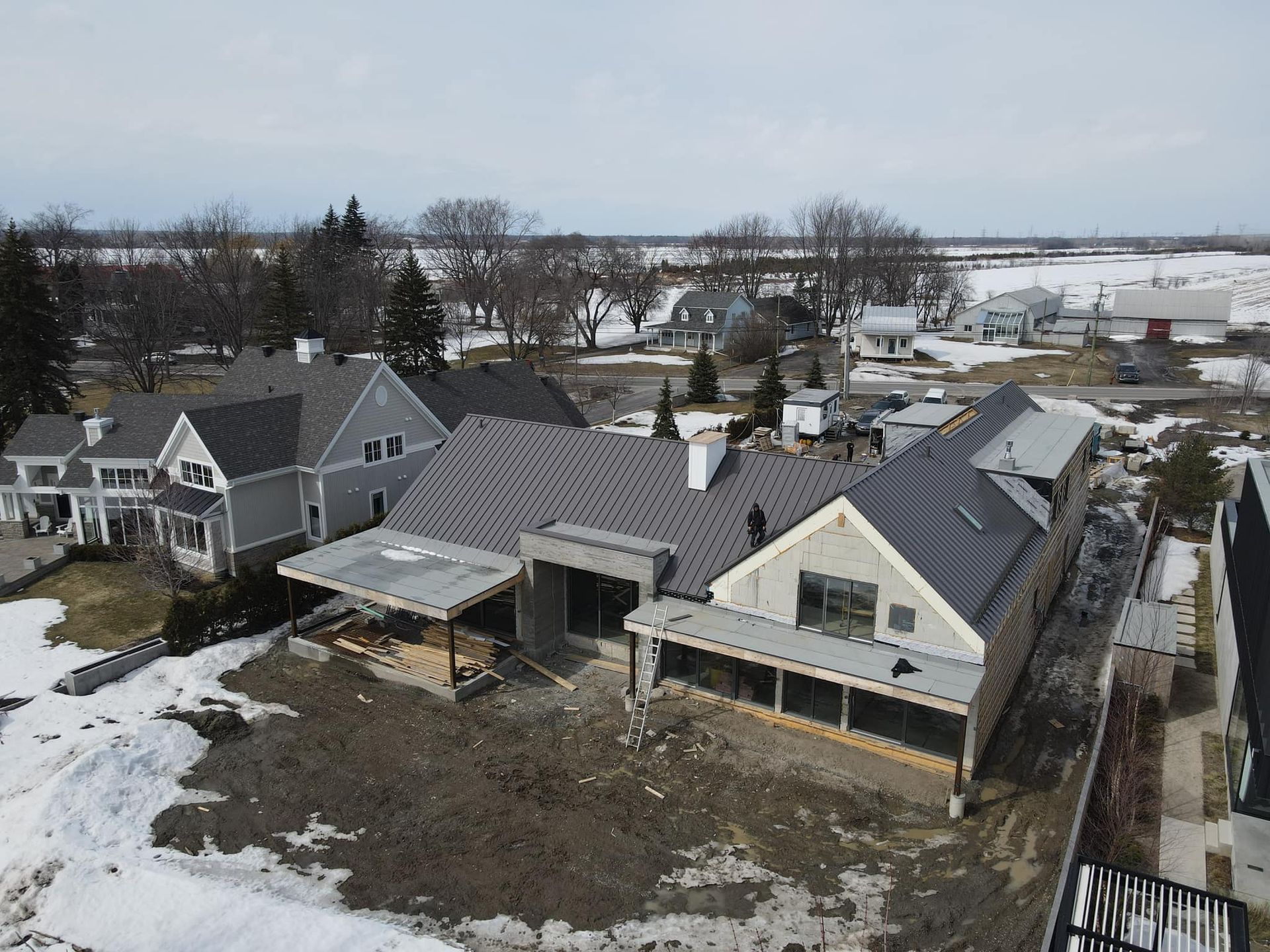 Vue aérienne de maisons enneigées et d'un quartier rural près de champs et d'un plan d'eau.