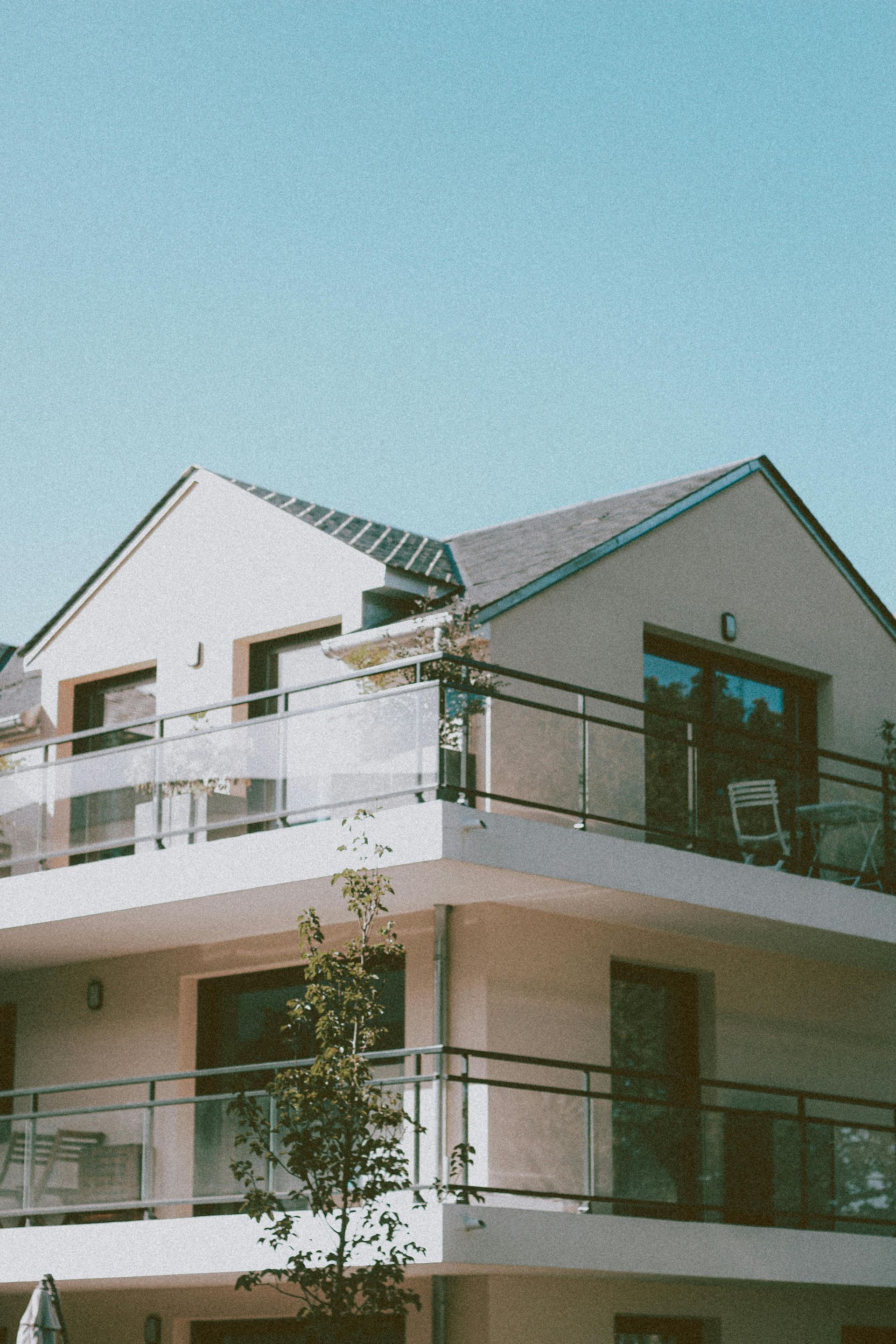Immeuble d'appartements moderne blanc avec balcons et toit vert sous un ciel bleu clair