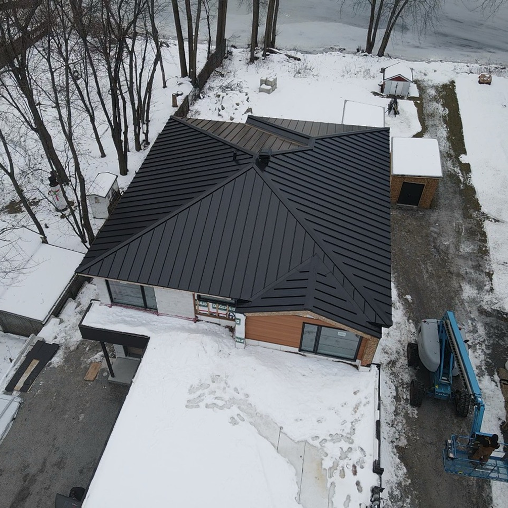 Maison enneigée au toit en métal sombre, vue du ciel en hiver.