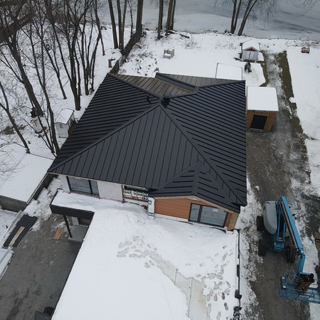 Maison enneigée au toit en métal sombre, vue du ciel en hiver.