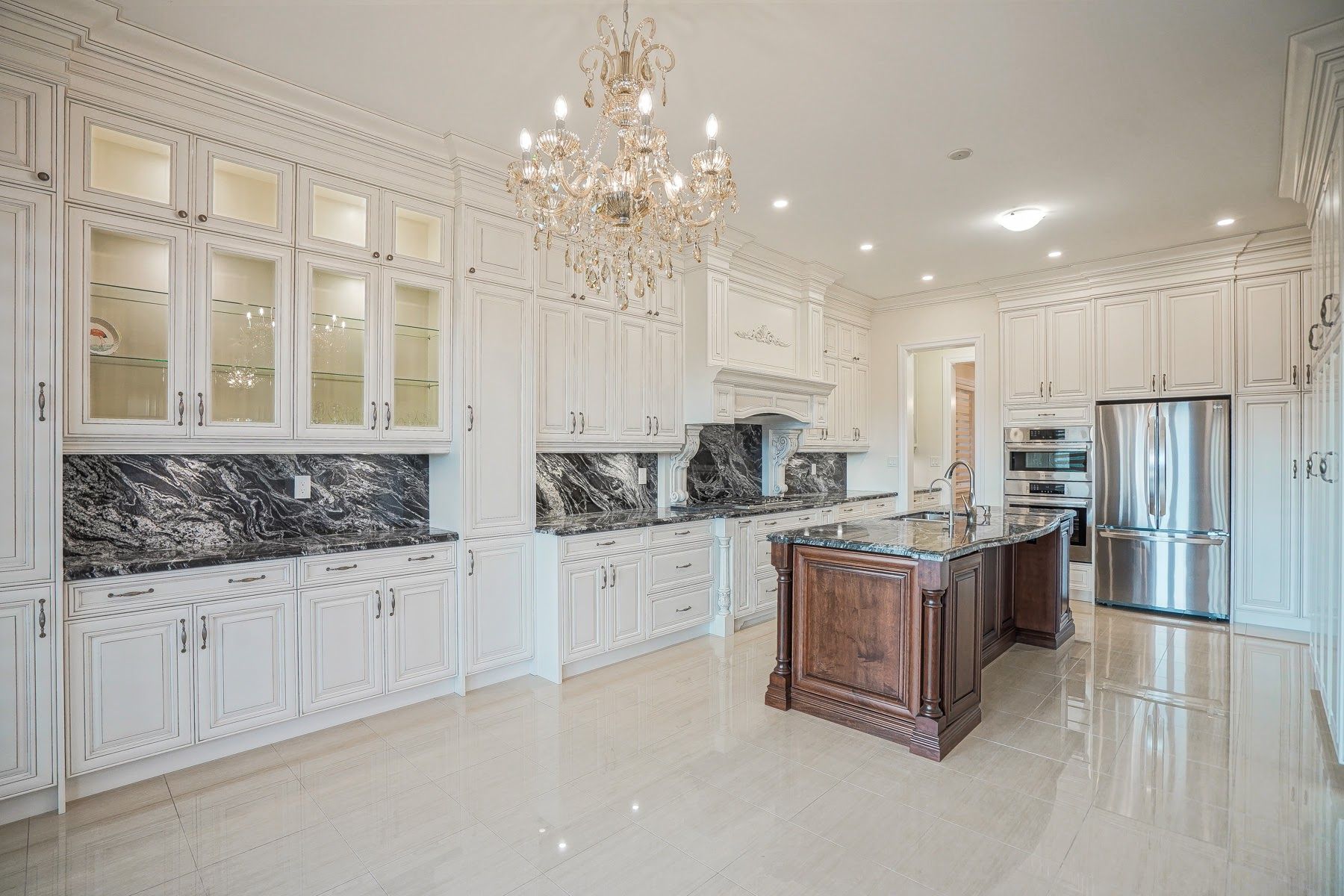 Elegant white kitchen with marble accents, chandelier, and stainless steel refrigerator