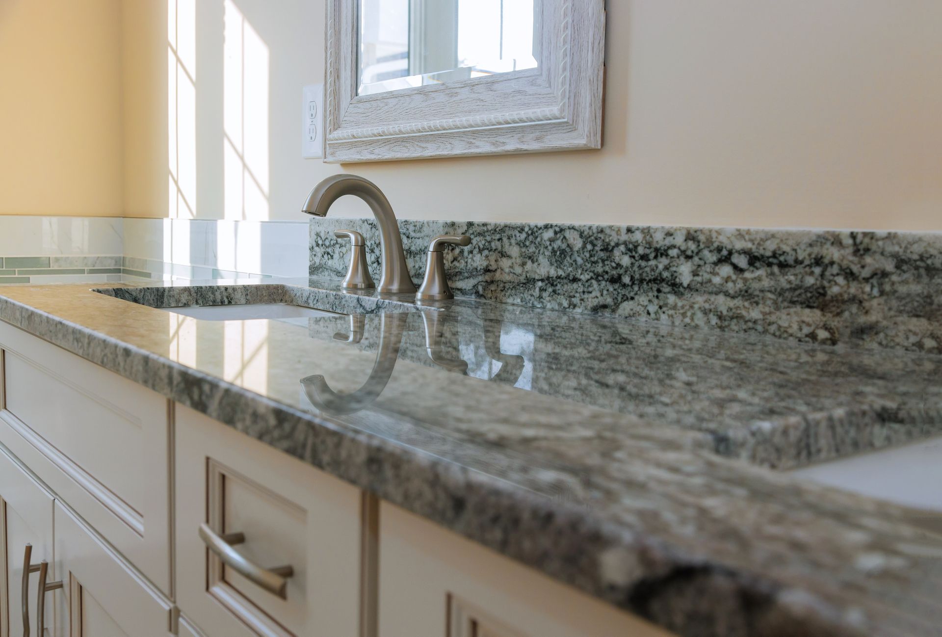 A vanity with a polished granite countertop and a bronze faucet, viewed at an angle in a light-colored bathroom.