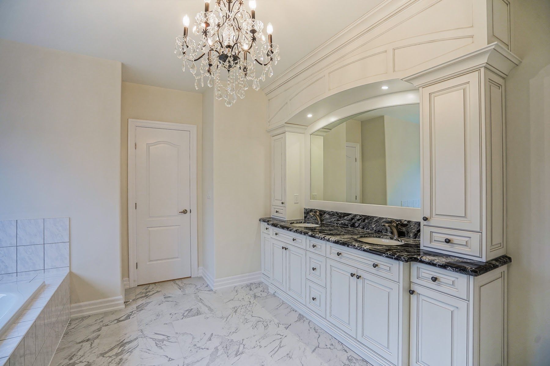 Elegant white marble bathroom vanity with chandelier, large mirror, and black granite countertop