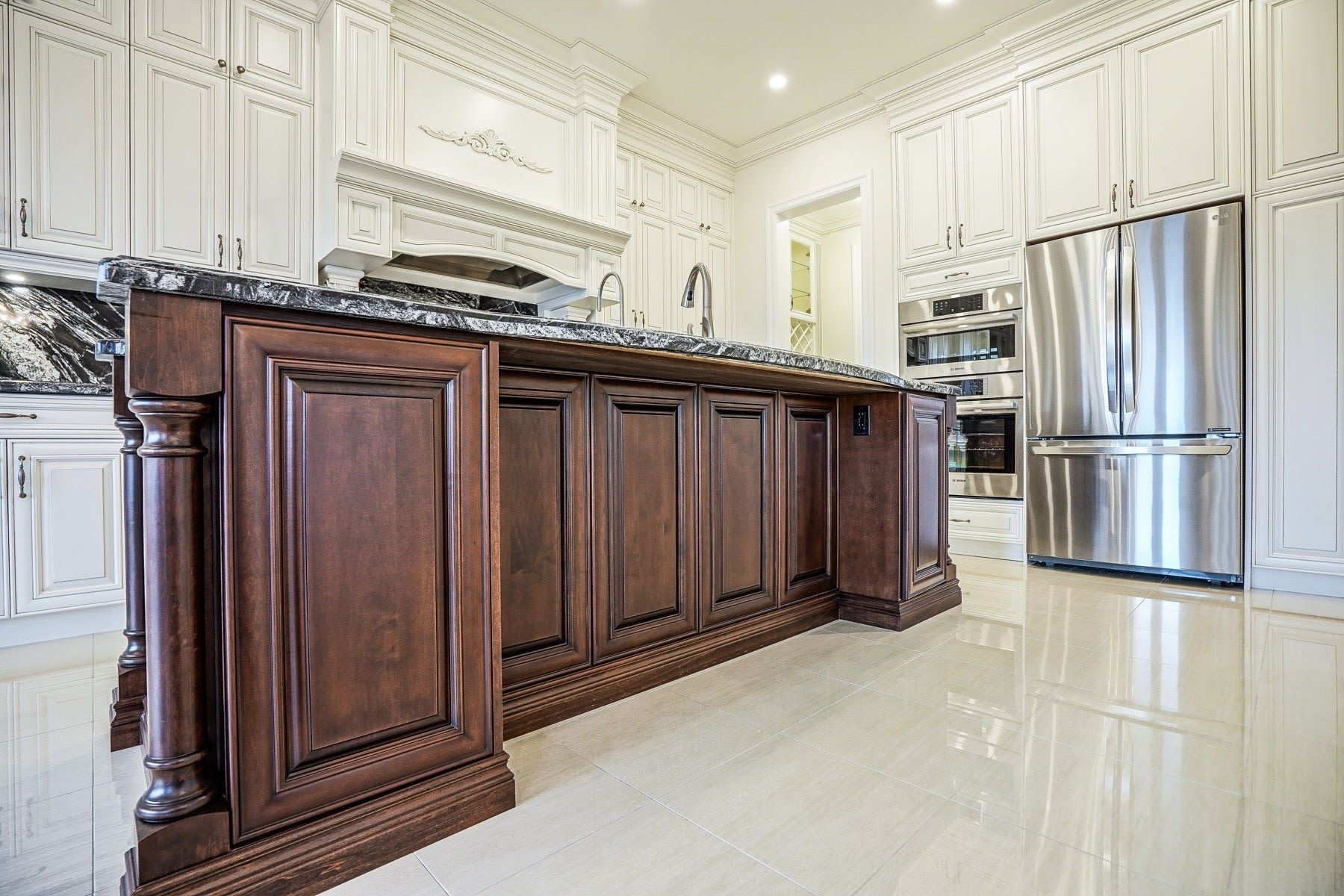 Bright kitchen with dark wood island, white cabinets, marble floor, and stainless steel refrigerator.