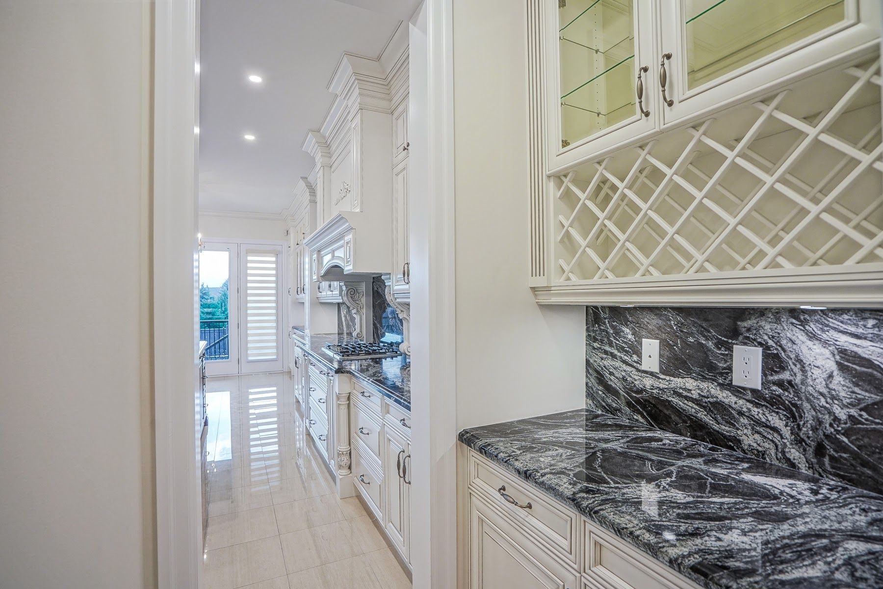 Bright white hallway kitchen with glossy marble counters, built-in cabinets, and lattice-front upper storage cabinetry