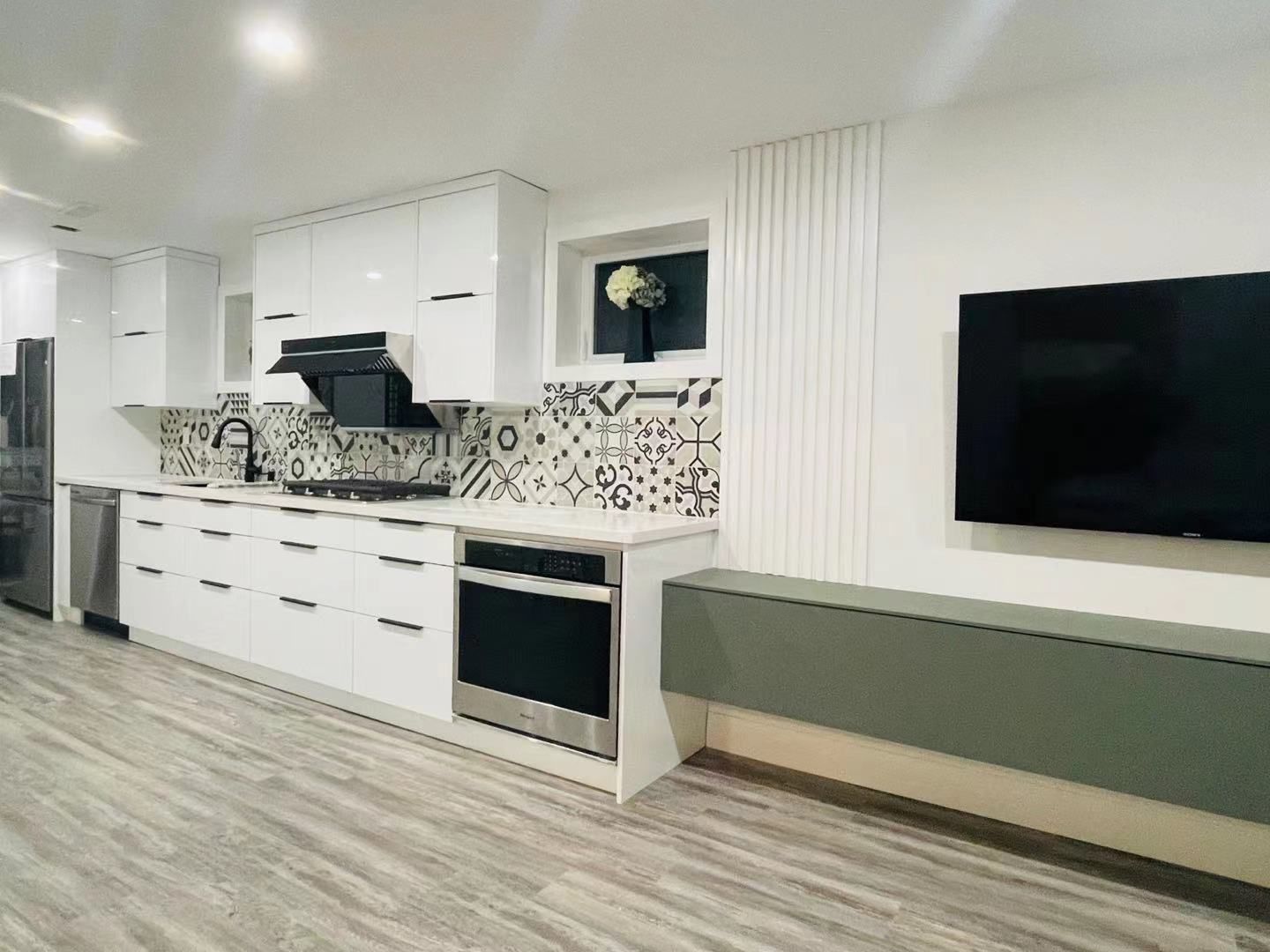Modern white kitchen and living area with black accents, patterned backsplash, and wall-mounted TV.