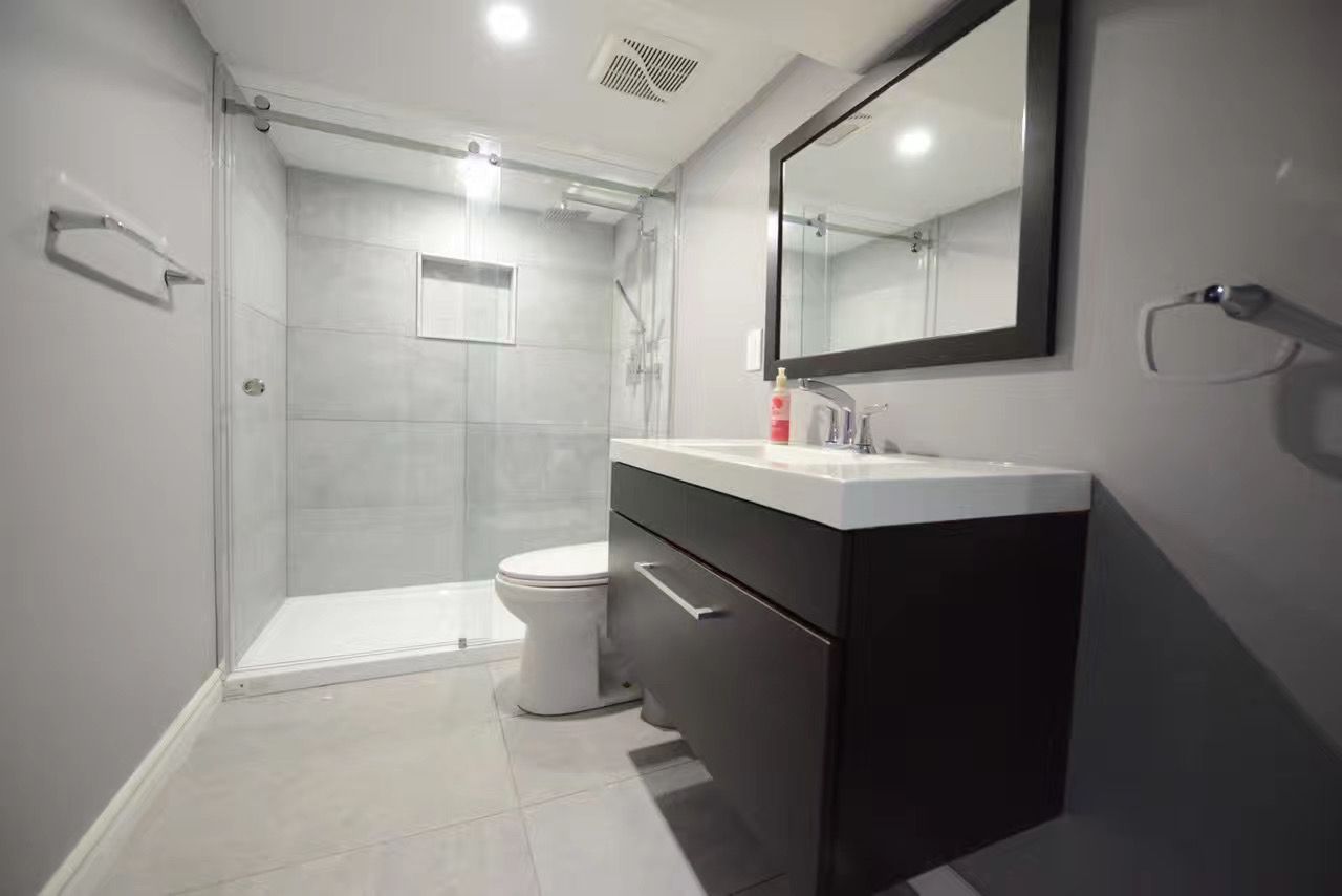 Modern bathroom with walk-in shower, toilet, dark vanity, and large mirror in gray tones