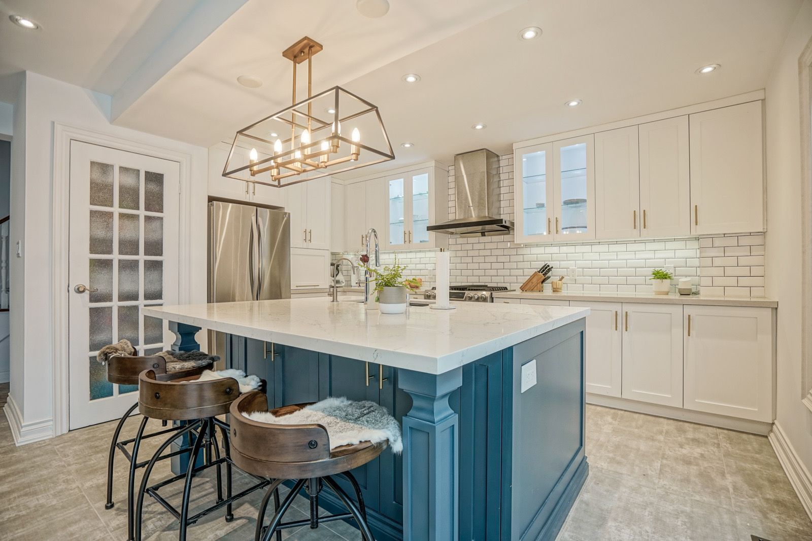 Bright modern kitchen with a large blue island, white cabinets, pendant light, and bar stools